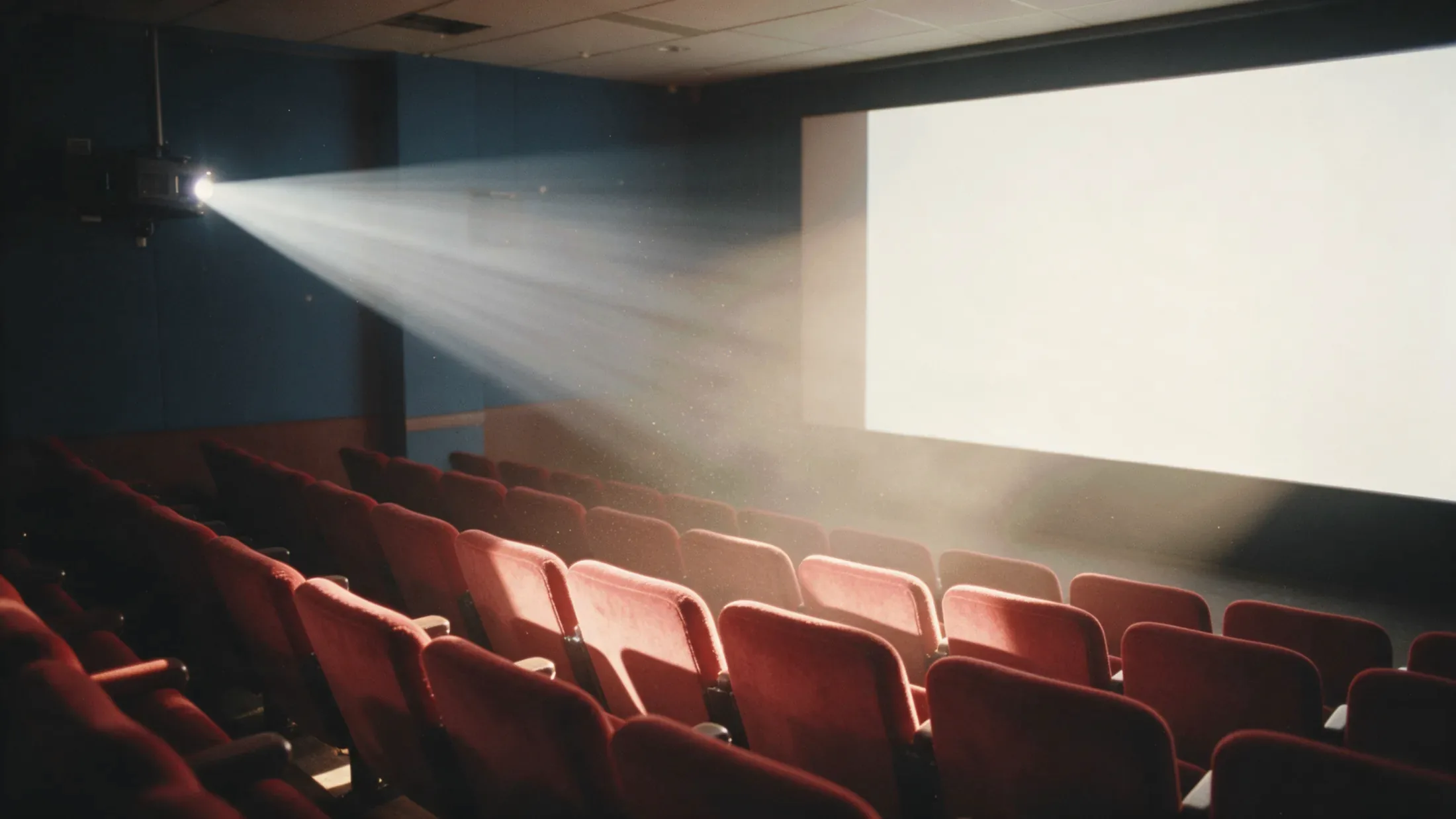 An empty cinema, a projector beam crossing toward a blank screen.