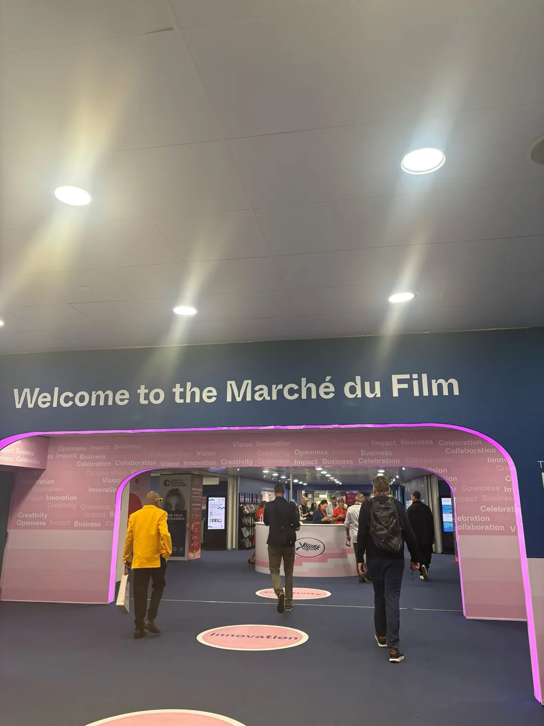 The pink and blue entrance arch to the Marché du Film, with visitors walking in.