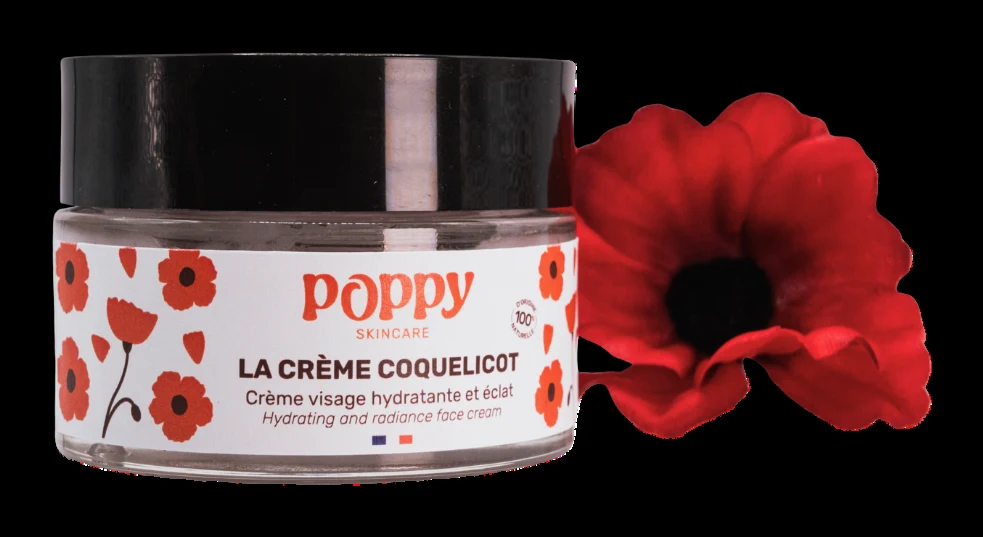 A jar of Poppy Skincare's poppy cream beside a red poppy flower.