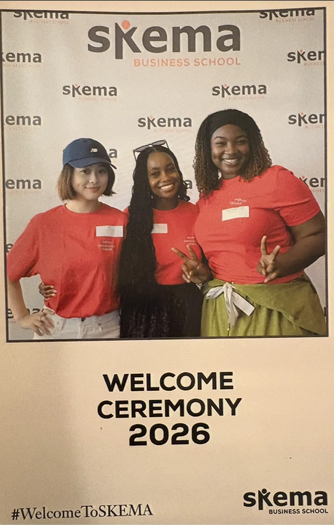 Yin Min with two other SKEMA orientation leaders in red t-shirts, posing at the SKEMA Welcome Ceremony 2026 photo wall.